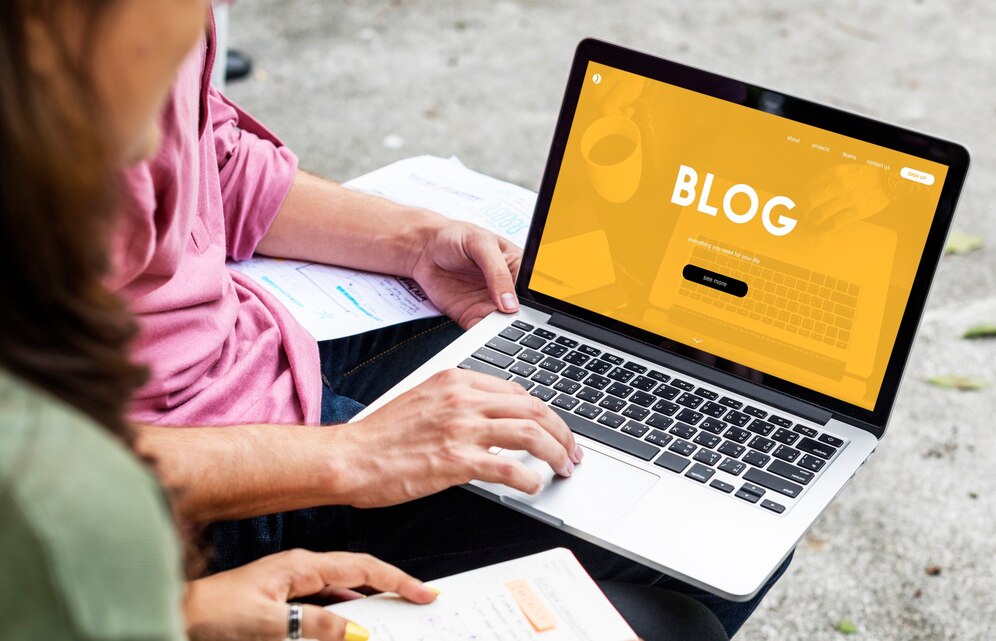 Two people are seated, with one using a laptop showing a "Blog" website. Another person is holding a notebook and pen, jotting down advertising strategies for their Inverness business.