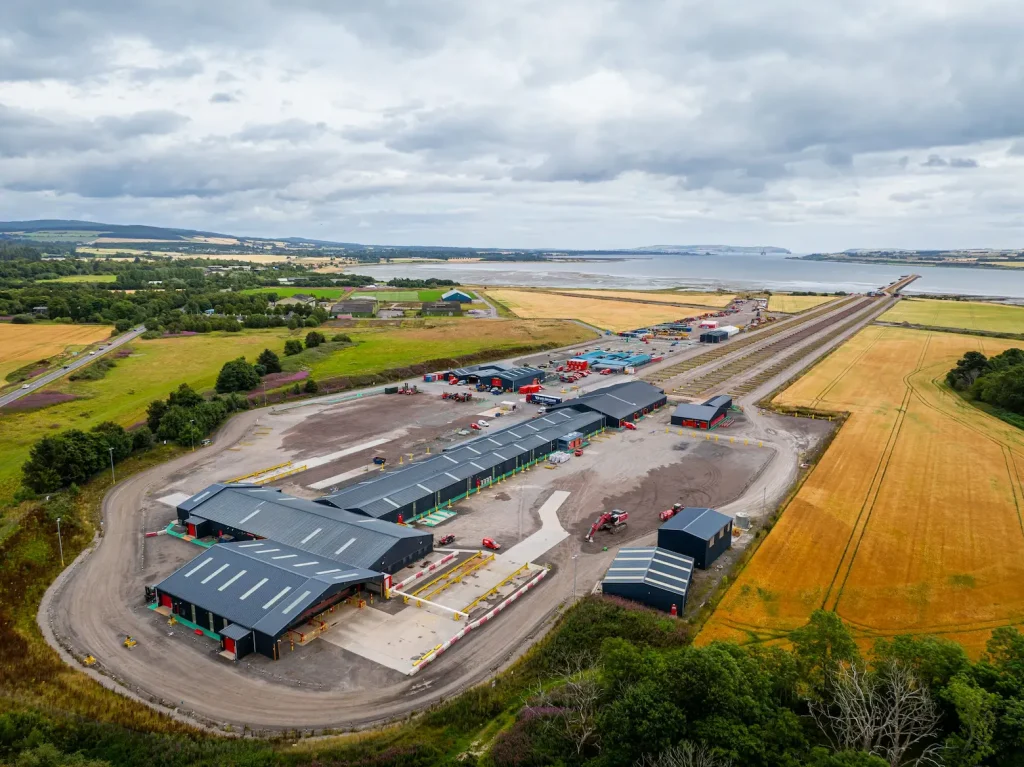 Aerial view of an industrial facility with multiple buildings and structures surrounded by fields near a body of water, under a cloudy sky, showcasing the strategic location of the Green Freeport.