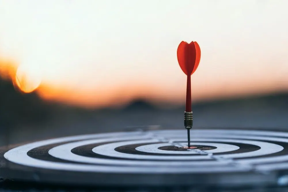 Close-up of a dart hitting the bullseye on a target board, symbolizing precision and success, much like Inverness's premier online marketing agency against the backdrop of a blurred sunset.